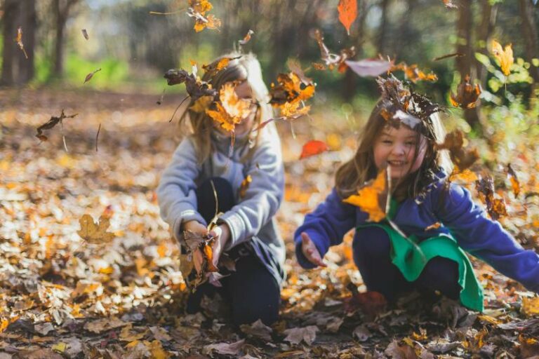 enfants jouant avec des feuilles mortes pendant les vacances de la Toussaint