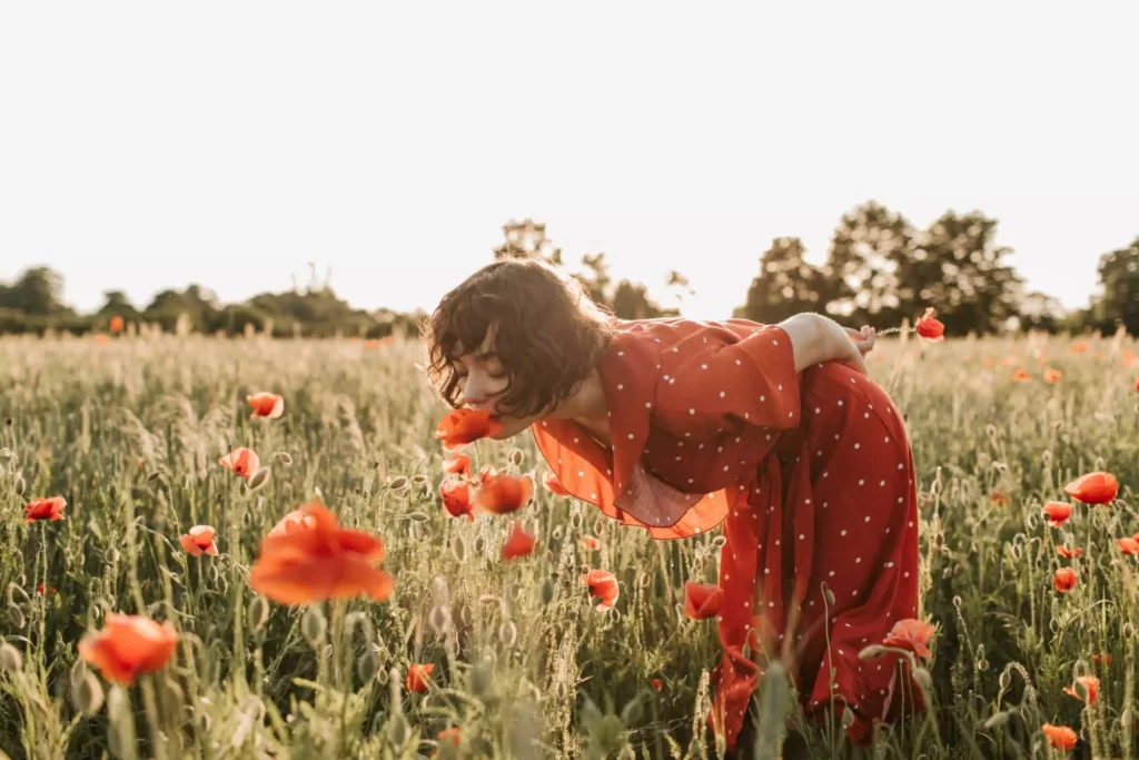 une jeune femme sent et observe des coquelicots en fleur dans un champ de céréales