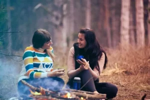 deux amies discutent autour d'un feu de camp au cours d'un séjour cocooning en famille en hiver chez Family Ecolodge Puisaye
