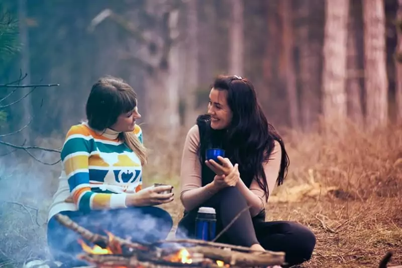 deux amies discutent autour d'un feu de camp au cours d'un séjour cocooning en famille en hiver chez Family Ecolodge Puisaye