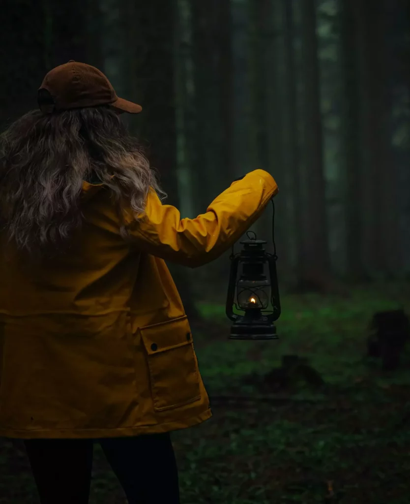 femme tenant une lampe dans la forêt, en pleine nuit.