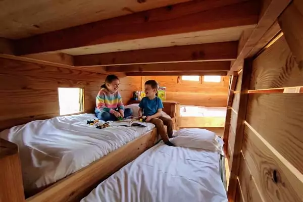 Des enfants jouent sur leur lit dans la cabane perchée dans les arbres.