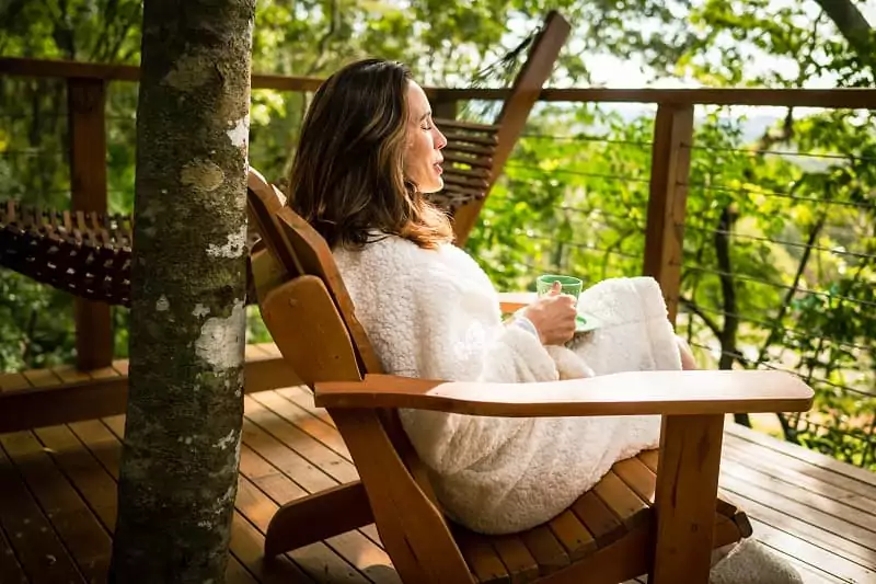 une maman se repose et boit un thé sur la terrasse de sa cabane perchée dans les arbres