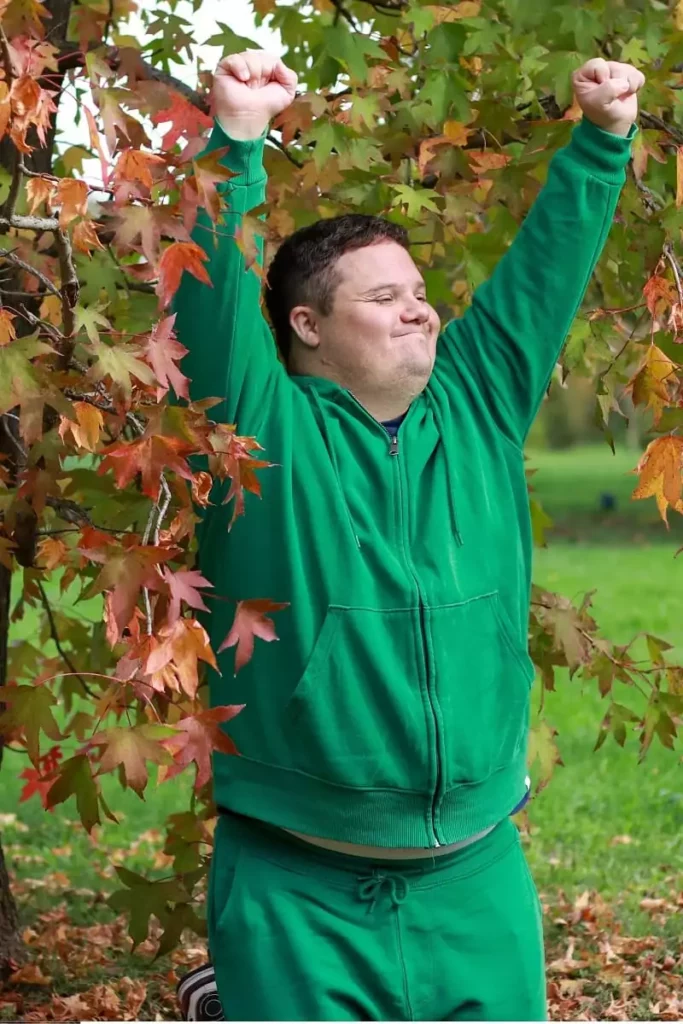 un jeune homme en situation de handicap lève les bras au ciel, avec le sourire, en signe de victoire