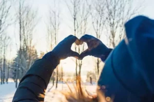 une femme forme un cœur avec ses mains face à un paysage hivernale de campagne pendant des vacances de février proche de Paris.