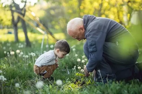 un enfant cherche des insectes dans l'herbe avec son grand-père, au cours du WE de Pâques