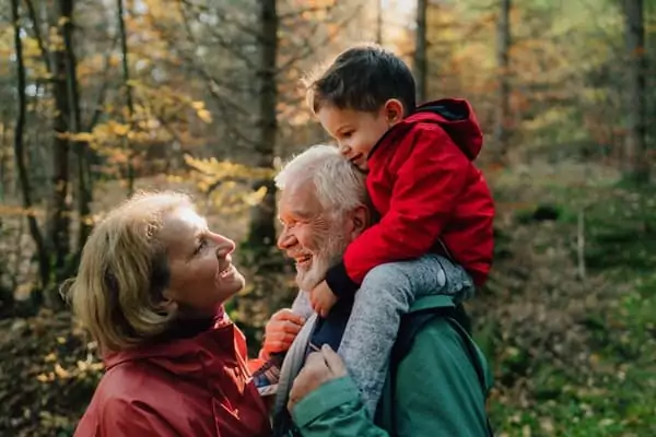 une couple de grands-parents profite d'une balade en forêt avec leur petit-fils de 3 ans sur les épaules du grand-père.