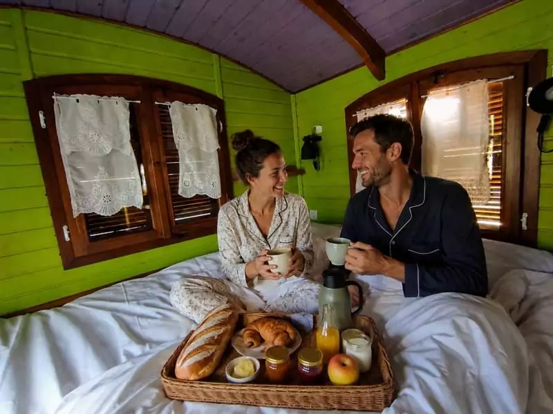 un couple prend son petit-déjeuner au lit en roulotte, à Family Ecolodge Puisaye