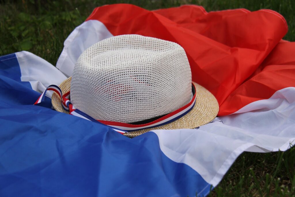 Un chapeau de paille posé sur une pelouse verte à côté d'un petit drapeau français évoquant une ambiance estivale de match de football de la coupe du monde.