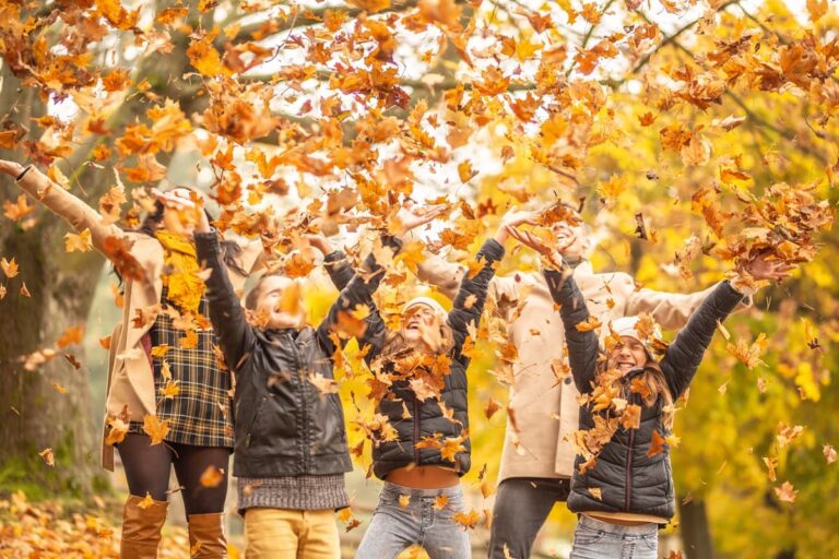 des enfants et leurs parents s'amusent en jetant en l'air des feuilles mortes, à l'automne et à la Toussaint