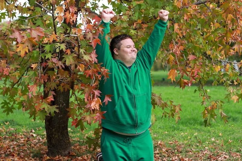 un jeune homme en situation de handicap est heureux, en pleine nature, en automne